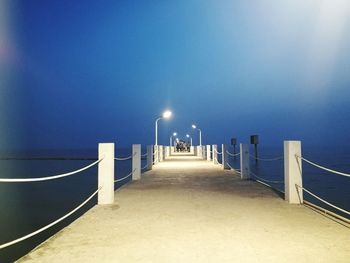 Illuminated pier over sea against clear sky at night