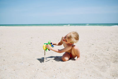 Boy sitting on beach by sea against sky