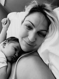 Portrait of smiling woman lying with toddler on bed