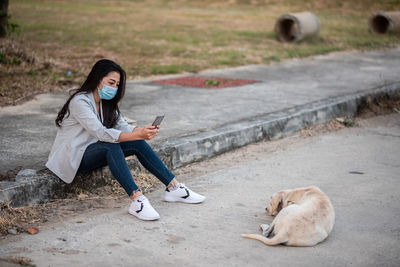 Full length of woman wearing mask photographing dog on road