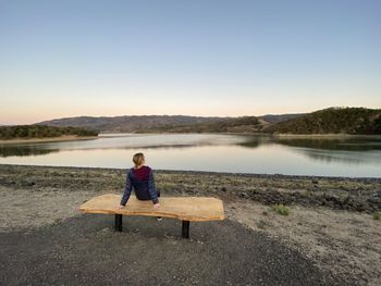 Rear view of woman sitting on seat by lake