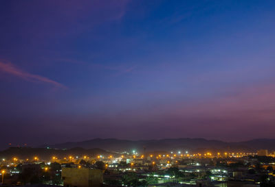 Illuminated cityscape against blue sky at night