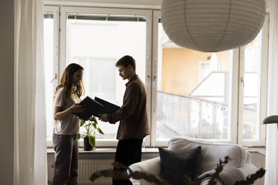 Couple holding agreement files while standing near window at new home