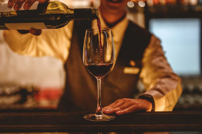 Midsection of man pouring wine in glass on table