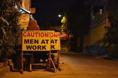 Information sign on road by buildings at night