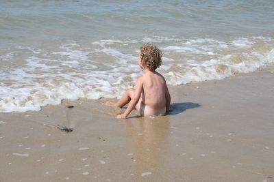 Rear view of shirtless boy on beach