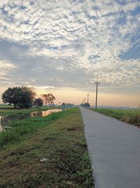 Road amidst field against sky during sunset