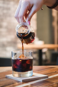 Midsection of person pouring drink in glass on table