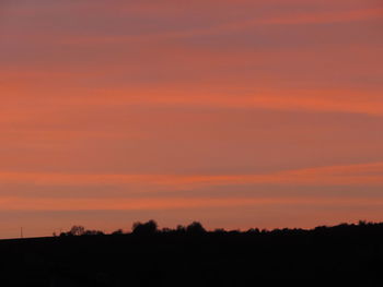 Silhouette trees on field against orange sky