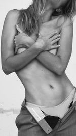 Midsection of shirtless woman standing against gray background