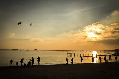 Silhouette people at beach against sky during sunset