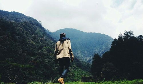Rear view of man standing on mountain against sky