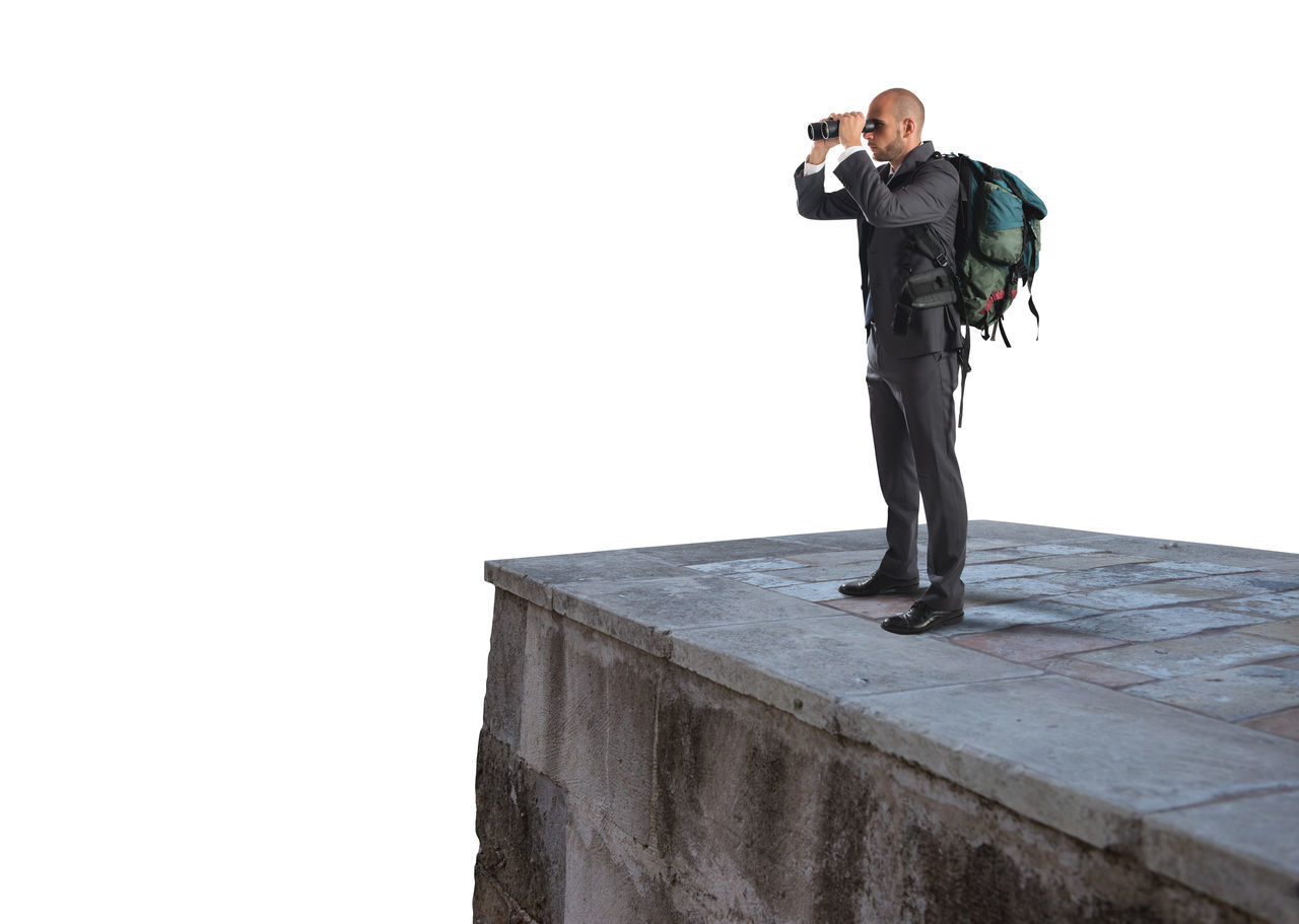 MAN HOLDING CAMERA WHILE STANDING AGAINST WHITE WALL