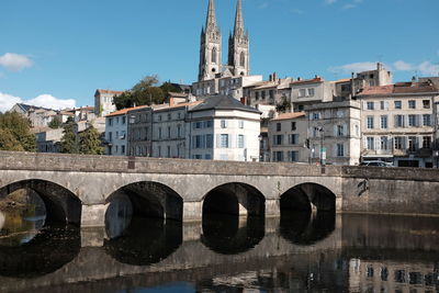 Arch bridge over river by buildings against sky