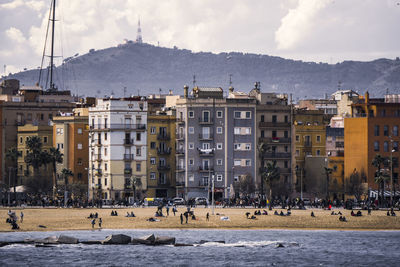 People at beach in city against mountains