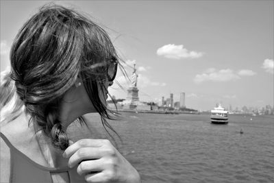 Mid adult woman looking at statue of liberty by river against sky