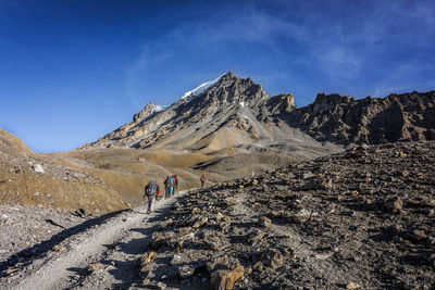 People walking on mountain against blue sky