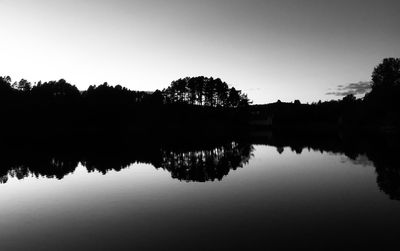 Silhouette trees by lake against sky