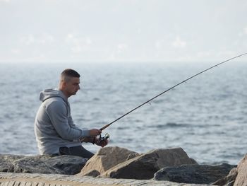 Man fishing on rock against sea