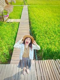 High angle portrait of young woman screaming while standing on boardwalk by plants