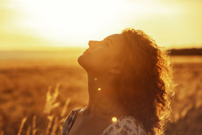 Young moroccan woman, with brown curly hair, in wheat field, sunset and blinding the camera