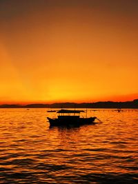 Silhouette boat in sea against orange sky