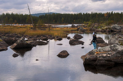 Girl standing at riverbank against cloudy sky