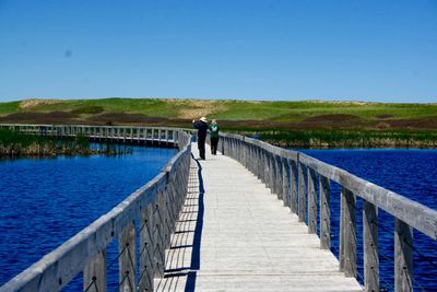 Man standing on pier over lake against clear blue sky