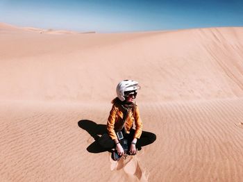 Woman sitting on sand at desert against sky