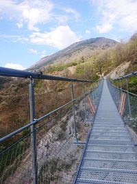 Footbridge leading towards mountains against sky