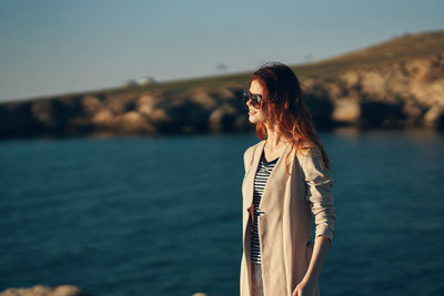 Woman wearing sunglasses standing by sea against sky