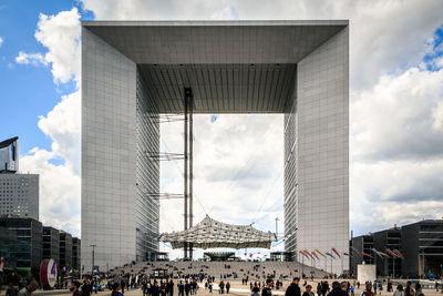 Group of people in front of buildings against cloudy sky