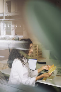 Side view of female architect comparing color samples while sitting at desk in office