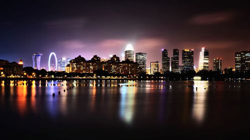 Illuminated buildings by river against sky at night