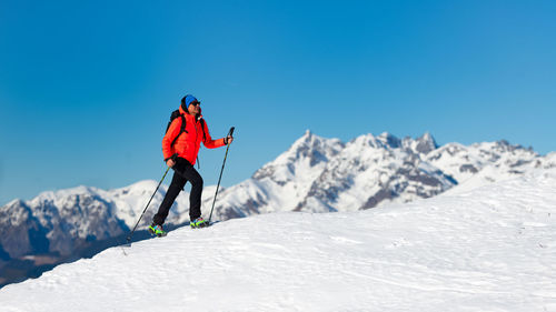 Man skiing on snowcapped mountains against clear blue sky