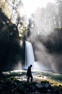 Man standing on rocks against waterfall in rainforest