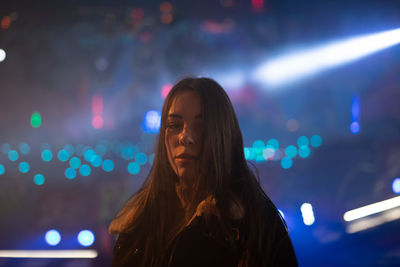 Portrait of woman standing against illuminated light at night