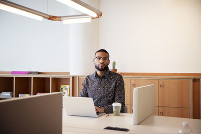 Portrait of businessman using laptop computer at table in office
