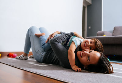 Happy woman laughing embracing adorable boy while lying on floor looking at camera in cozy room at home