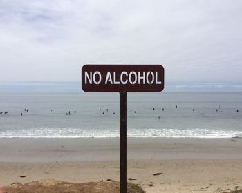 Information sign on beach against sky