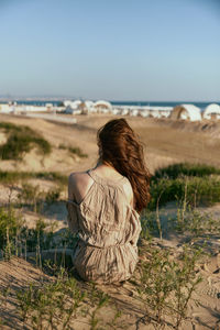 Rear view of woman sitting at beach against sky