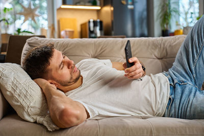 Young woman using mobile phone while lying on bed at home