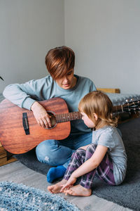 Young woman playing guitar while sitting on carpet at home