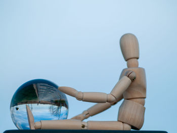 Low angle view of wooden figurine by crystal ball against clear sky