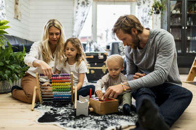 Woman teaching abacus to daughter while man playing with son in living room at home