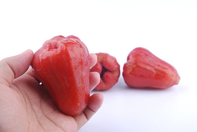 Close-up of hand holding strawberry over white background