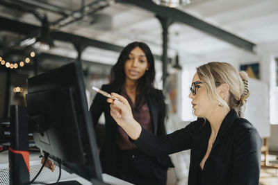 Young businesswoman explaining female colleague over desktop pc at office