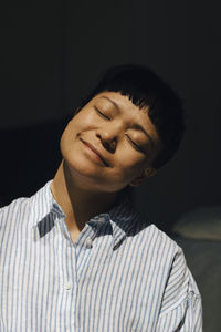 Smiling young woman with eyes closed in sunlight