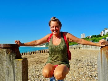 Portrait of smiling woman crouching at beach against clear sky