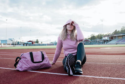 Woman sat on a running track looking tired and thinking